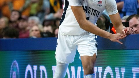 A bearded man in classes and a white speckled shirt holds a rainbow colored U.S. flag.