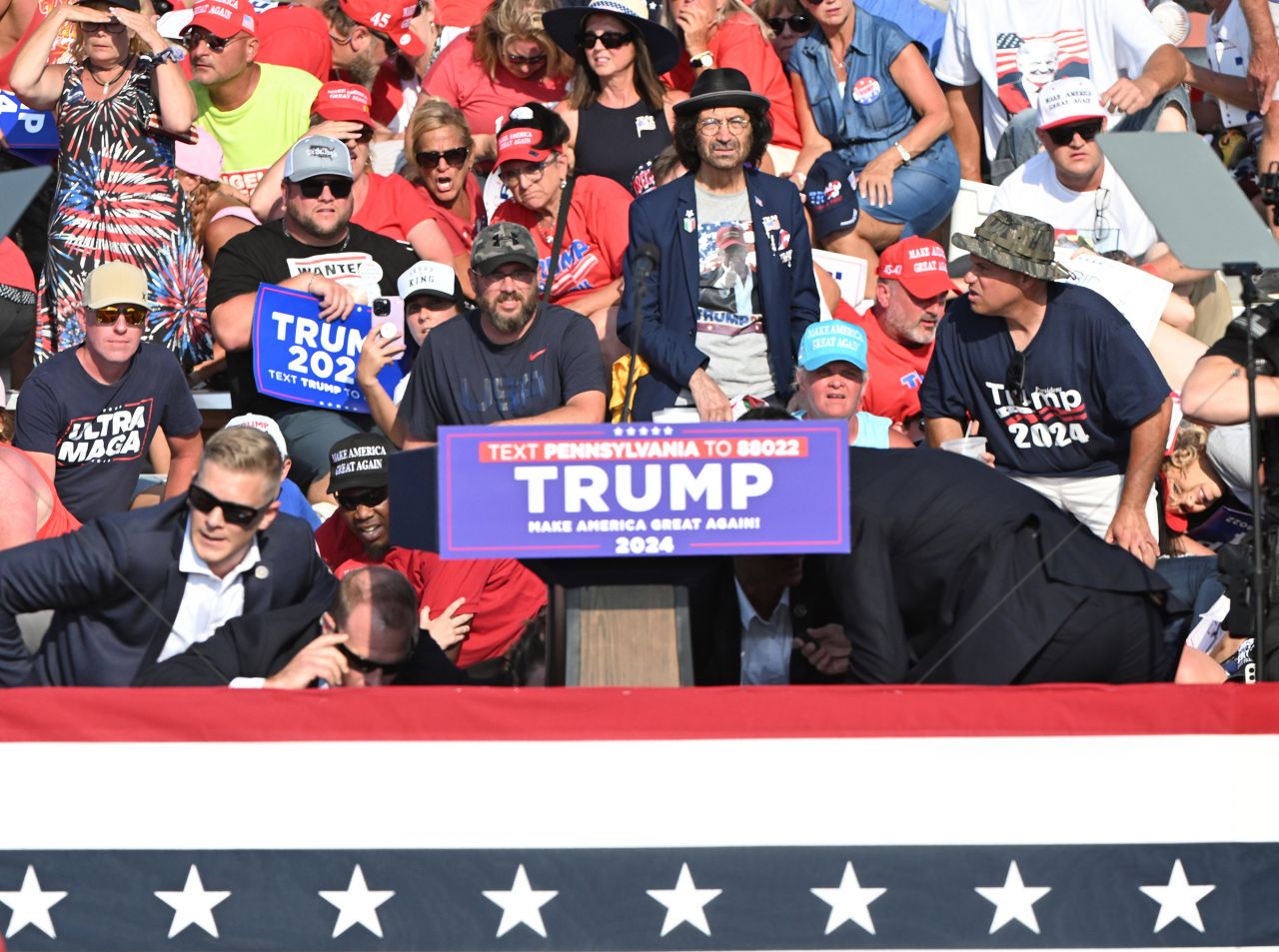 People look at a podium with others crouched under it