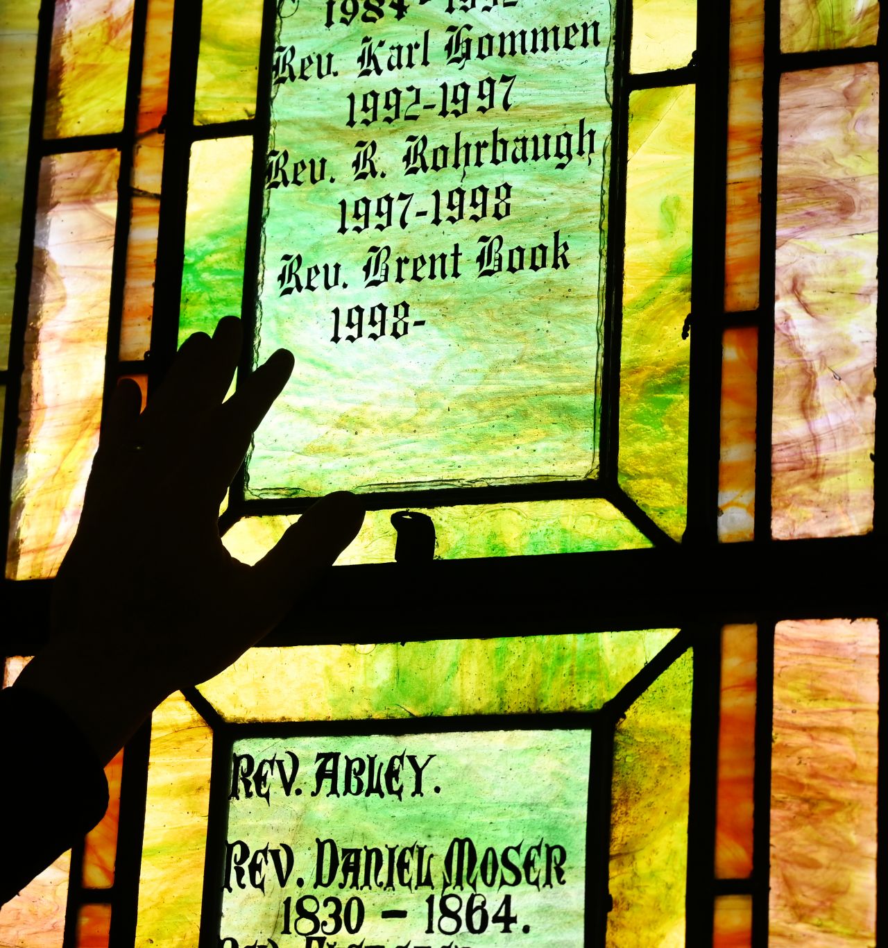 A close-up of a person's left hand against text on a stained-glass window.
