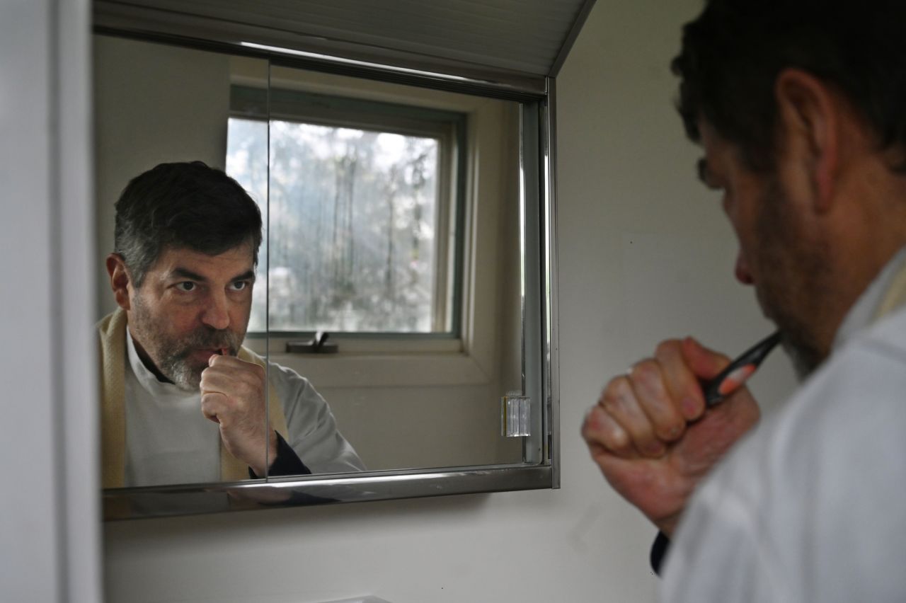 A dark-haired man looks at his reflection in the mirror as he brushes his teeth.