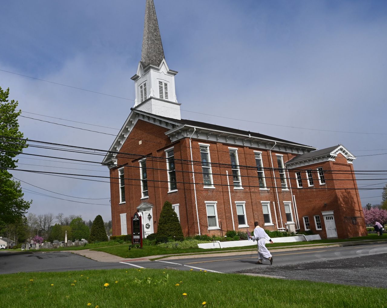 A man in a white robe approaches a two-story brick church.