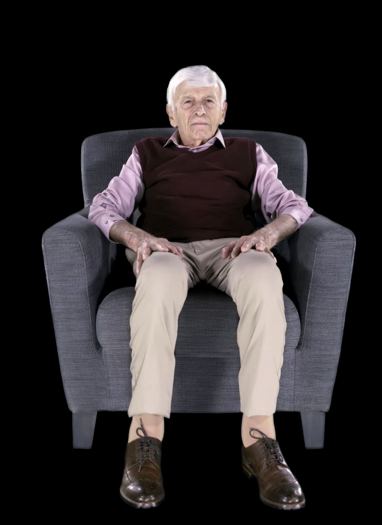 Gray haired man in a sweater vest seated in a comfy chair.