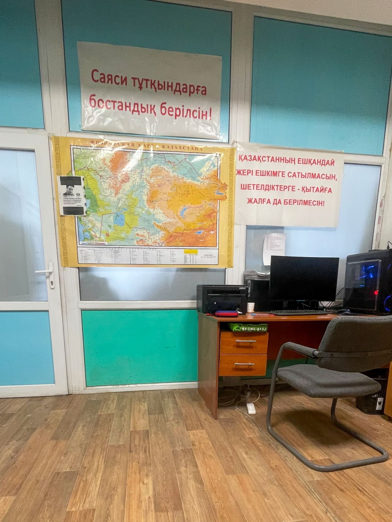 On the walls are two posters. One on the left says, “Let political prisoners be freed.” The other, on the right, says, "No land in Kazakhstan should be sold or leased to foreigners or to China."