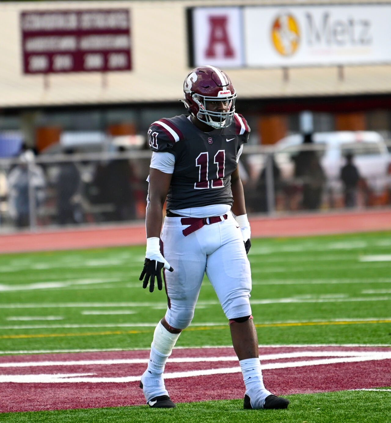 A football player wearing a dark gray jersey with number eleven and a maroon helmet celebrates on a football field.