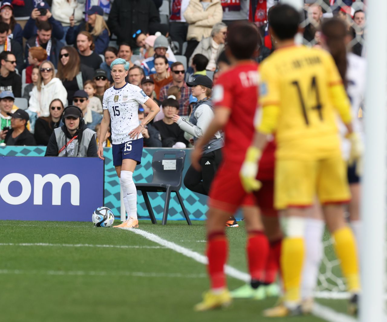 A women's soccer player in a white uniform looks out at the field before attempting a corner kick.