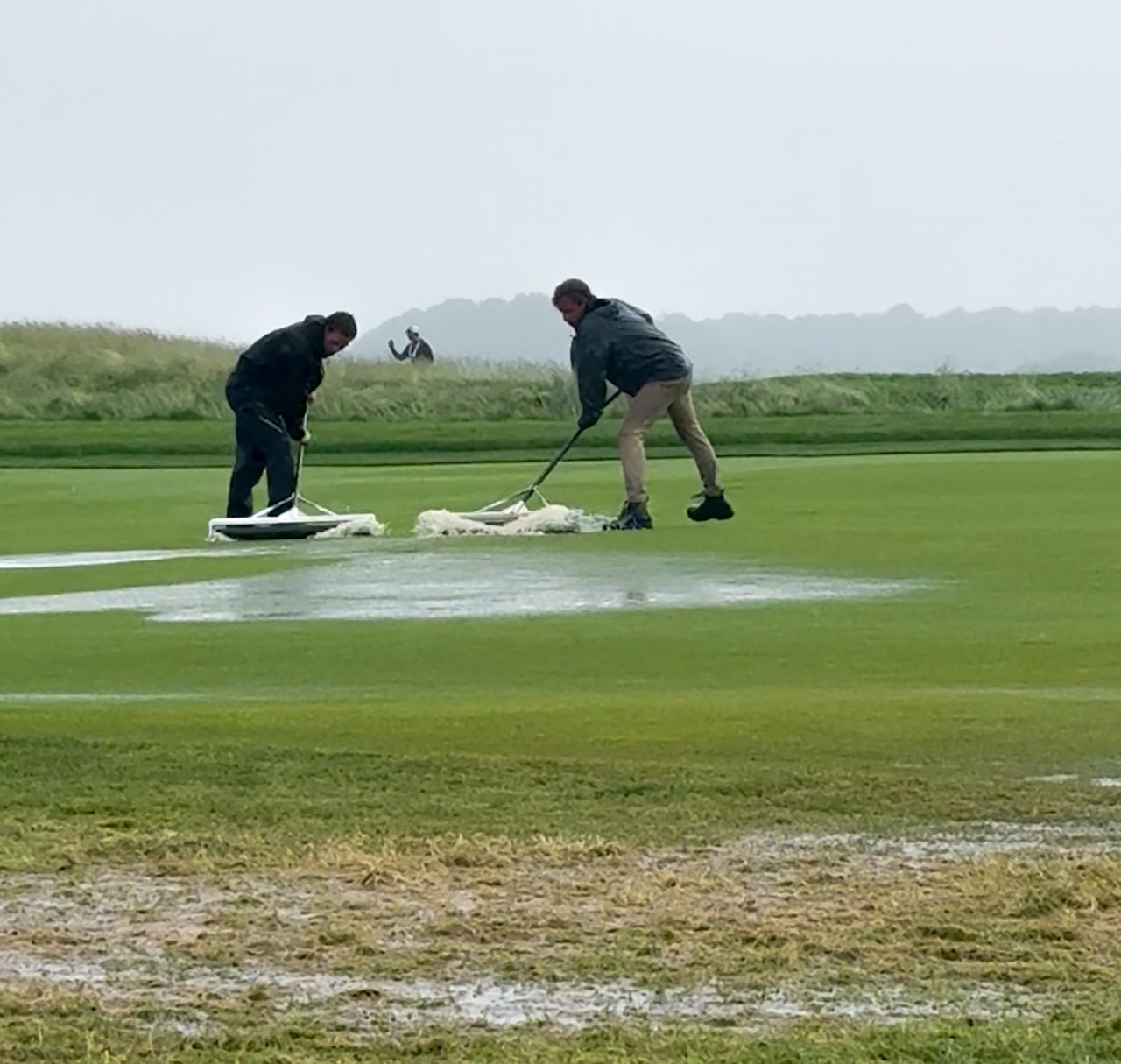 Two men clear water from a golf green