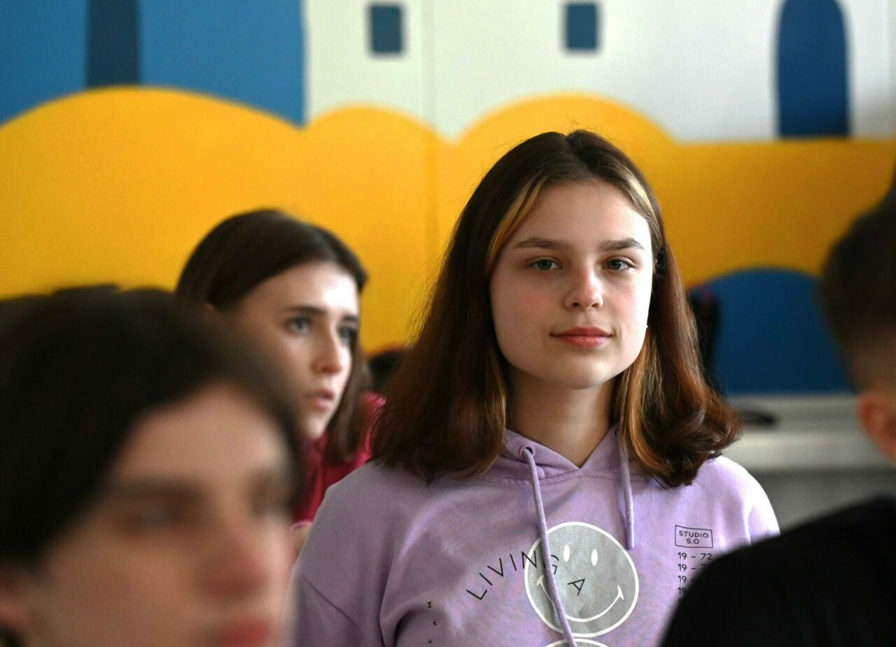 Brown haired student in pink hoodie looks at camera.