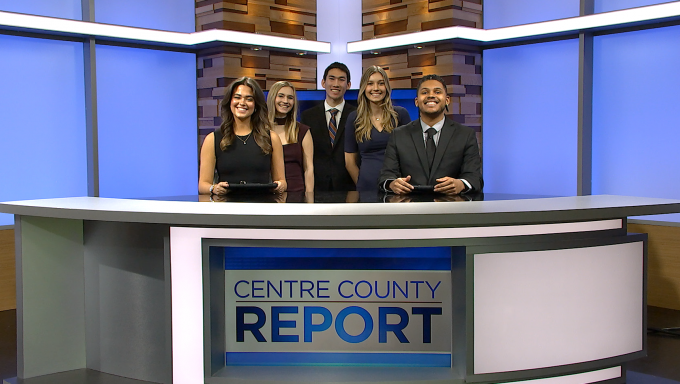 two young men and three young women standing behind a news anchor desk