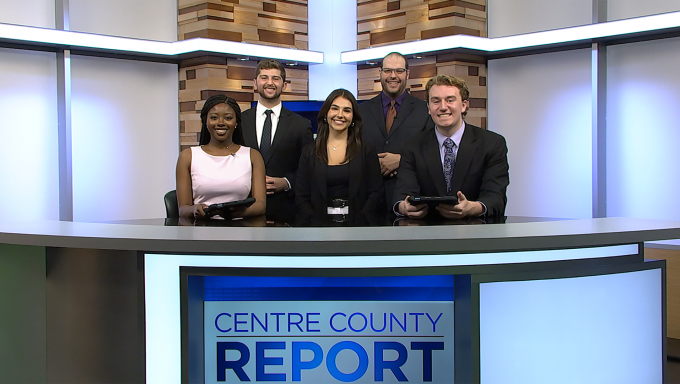 Five Centre County Report reporters and anchors standing behind the Centre County Report anchor desk