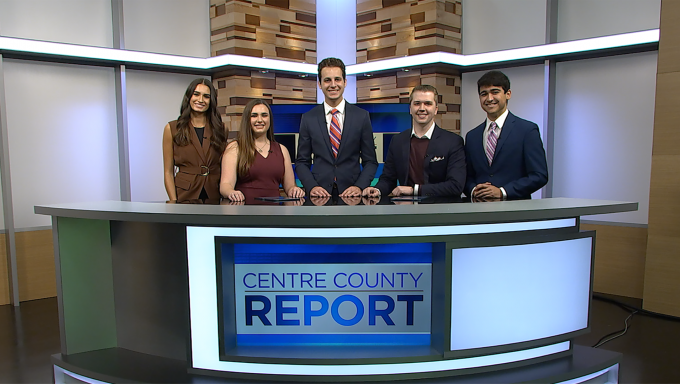 five Centre County Report news and weather anchors standing behind the Centre County Report news desk