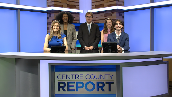 five news, sports and weather anchors standing behind a news desk