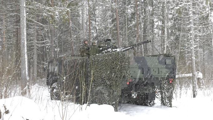 Members of the Estonian Defense Force on an armored personnel vehicle in the woods with snowfall