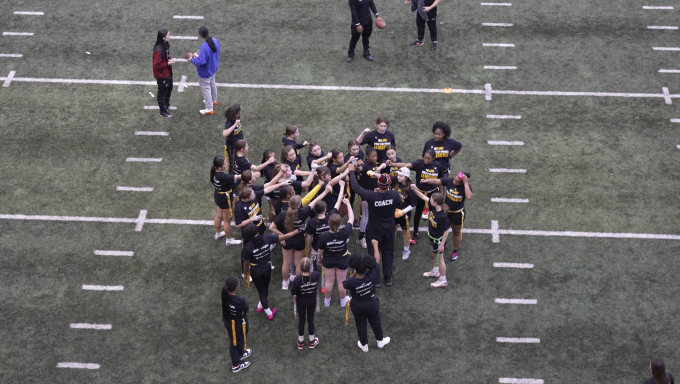 Multiple girls flag football players breakdown a huddle ahead of their jamboree.