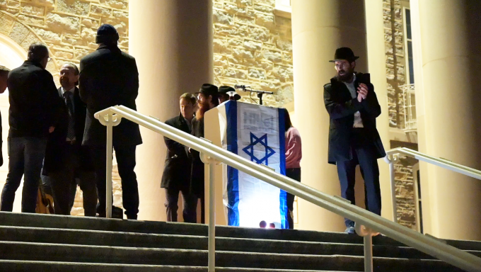 several rabbis standing at a podium at night