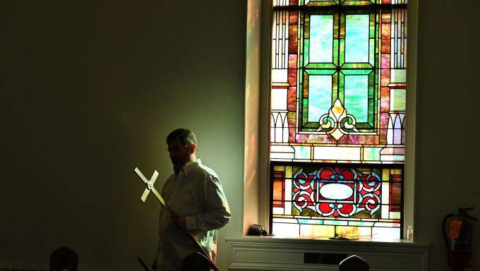 A man in a white shirt walks in front of a stained glass window.