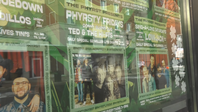 a picture of a band poster taped on local whiskey's window to promote the live bands at the Phyrst