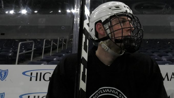 A club Penn State hockey player sits in the players bench area watching practice.