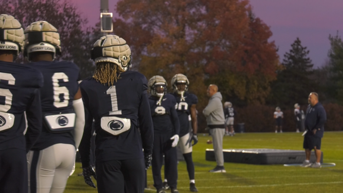 Several Penn State Football players stand on the left as they prepare for a drill at dusk.