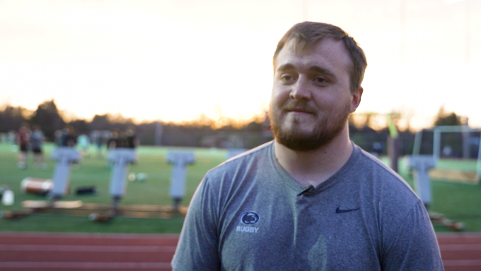 Rugby Coach Toby Brennan with rugby practice field behind him.