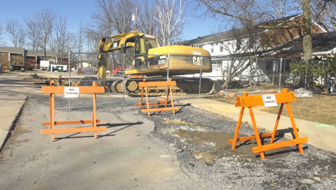 A sinkhole in front of an apartment complex with heavy machinery and no parking signs