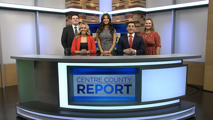 Five Centre County Report news anchors and reporters standing behind their anchor desk