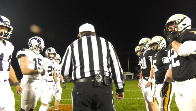 Tyrone and Penns Valley high school football players facing off on a football field for a coin toss with a referee in the foreground