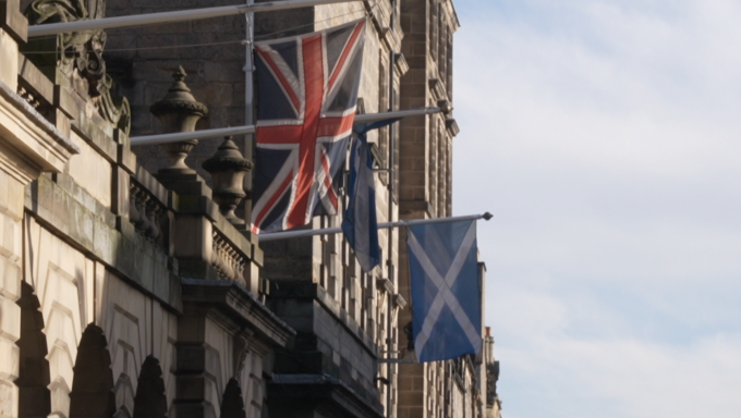 A photo of a Scottish and Union Jack flag next to each other hanging from a building.