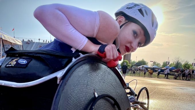 Esther-Faith is in her wheelchair looking over her right wheel at the track with a sunset in the background