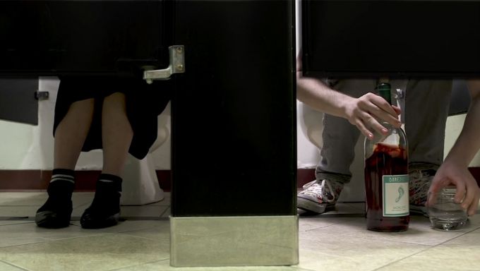 The legs of two people seen under bathroom door stalls.