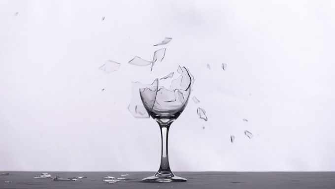 A wine glass in front of a white background is shattering into pieces