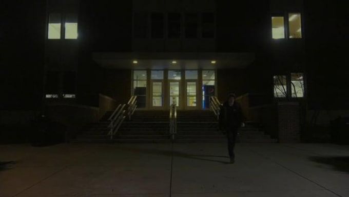 A student on a very dark campus walks away from a dimly lit building