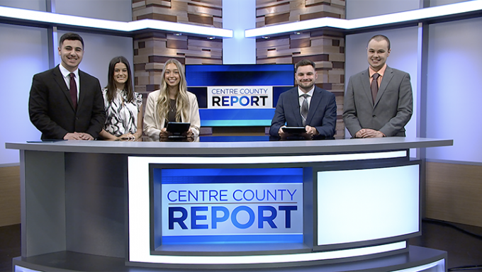 a picture of five news anchors standing behind a news desk