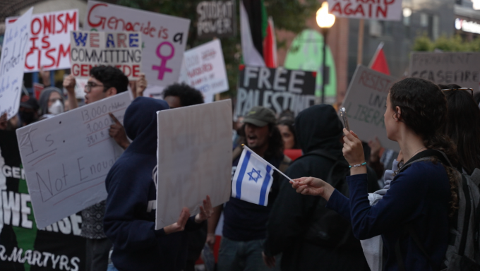 Israel supporter waves flag in front of passing pro-Palestine protestors.