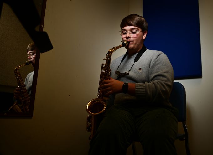 Dark haired man with glasses playing a saxaphone
