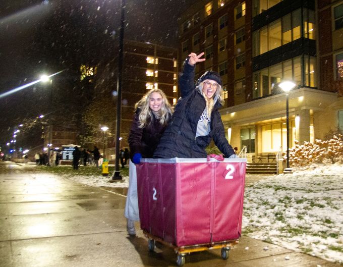 One woman pushing another in a red cart