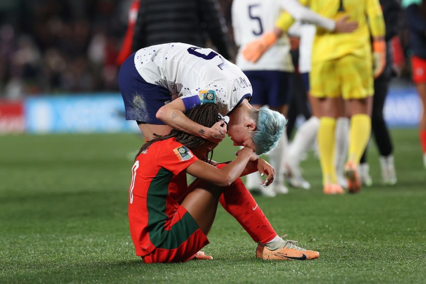 Soccer player consoles another who's sitting on the grass