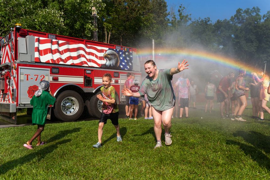 Children run in the rainbow spray of a water hose